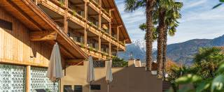 Außenaufnahme Mondi Hotel Tscherrms mit Palmen und Bergpanorama